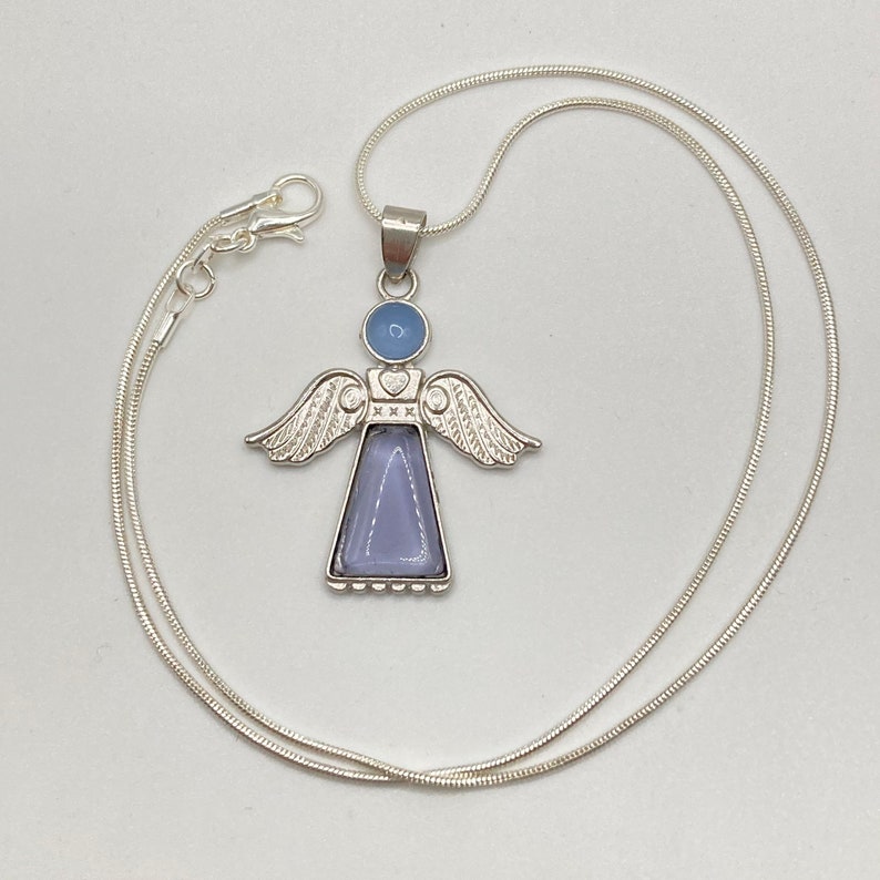 Op de afbeelding: Een zilveren ketting met een engelhanger. De engel is gemaakt van zilver en heeft een blauw glazen lichaam. De vleugels van de engel zijn versierd met een zilveren ontwerp.