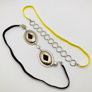 May include: A silver headband with two decorative silver charms and a yellow elastic band.