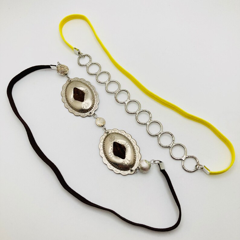 May include: A silver headband with two decorative silver charms and a yellow elastic band.
