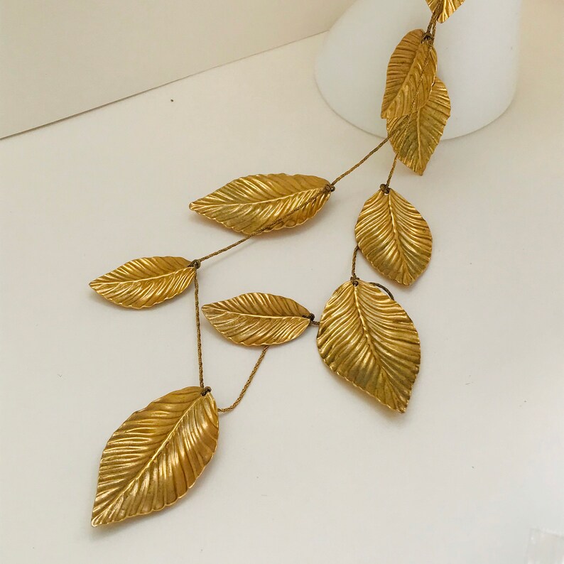 May include: A gold leaf necklace with a long chain and multiple leaves hanging from it. The leaves are textured and have a metallic finish.