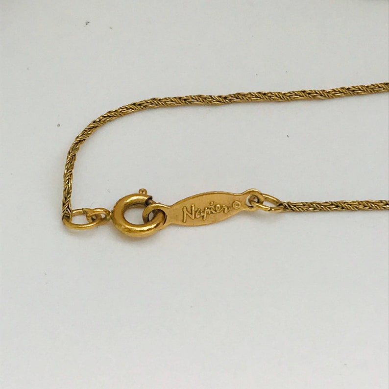 May include: A gold chain necklace with a clasp and a tag that reads "Napier".