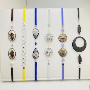 May include: Seven decorative hanging ornaments with tassels. The ornaments feature a variety of designs, including floral, geometric, and abstract patterns. The ornaments are made of metal, glass, and beads. The tassels are made of various colors, including blue, white, yellow, and black.