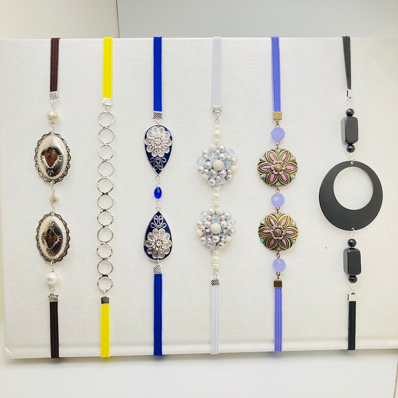 May include: Seven decorative hanging ornaments with tassels. The ornaments feature a variety of designs, including floral, geometric, and abstract patterns. The ornaments are made of metal, glass, and beads. The tassels are made of various colors, including blue, white, yellow, and black.
