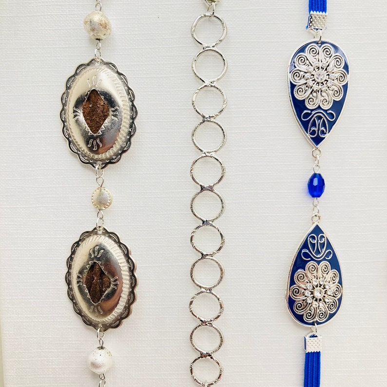 May include: Three silver chains with pendants. The chains are made of linked circles. The pendants are silver with blue enamel and intricate designs. The pendants are shaped like teardrops and have a floral pattern.