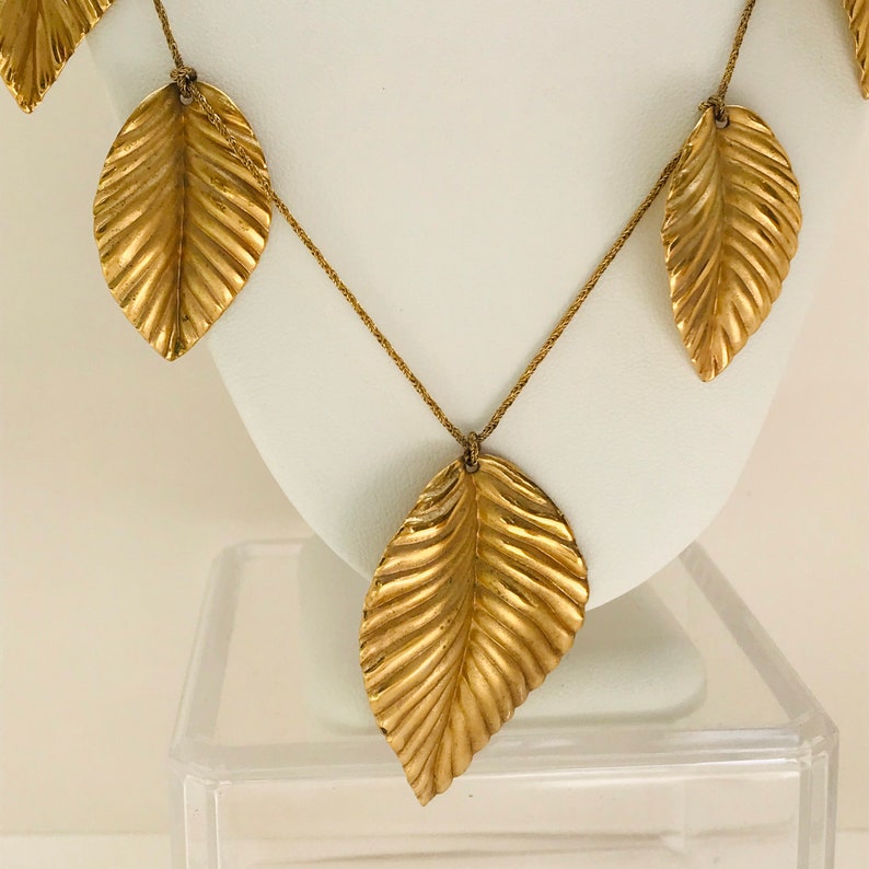 May include: A gold necklace with multiple leaf-shaped pendants. The leaves are textured and have a slightly raised design.