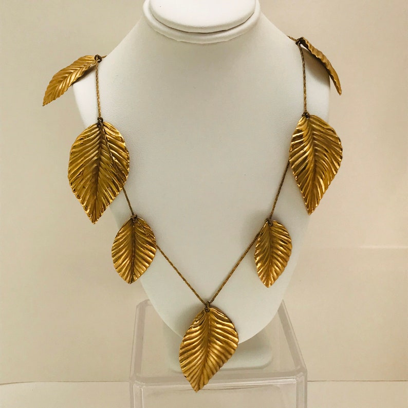 May include: A gold necklace with a chain and multiple leaf-shaped pendants. The leaves are textured and have a slightly hammered look.
