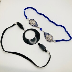 May include: Two headbands with black and blue accents. One headband is black elastic with a black circle and black and blue beads. The other headband is blue elastic with two silver and blue teardrop-shaped pendants.