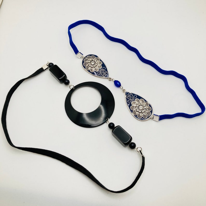 May include: Two headbands with black and blue accents. One headband is black elastic with a black circle and black and blue beads. The other headband is blue elastic with two silver and blue teardrop-shaped pendants.