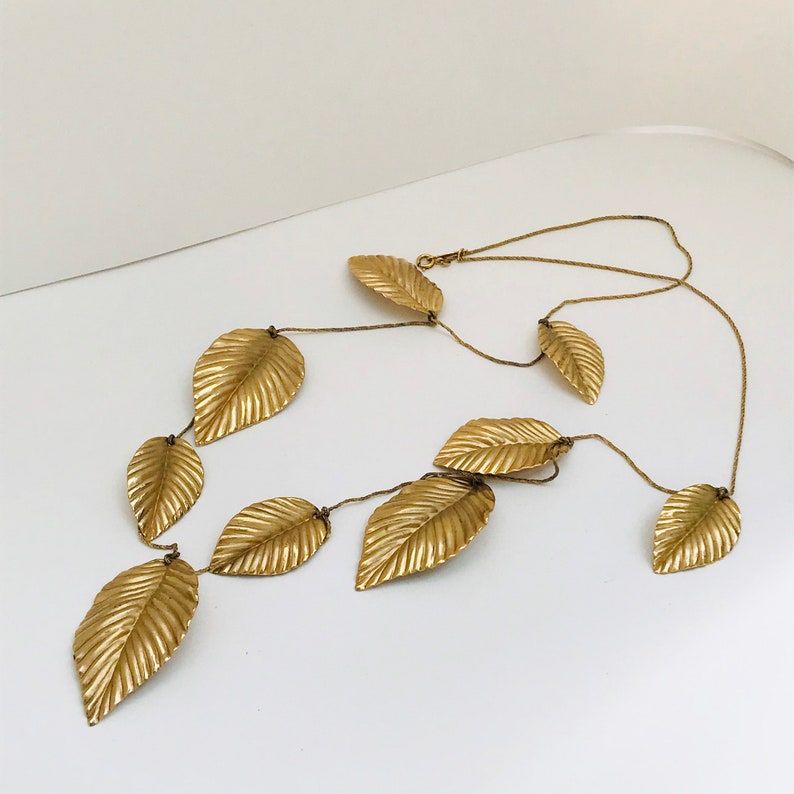 May include: A gold necklace with multiple leaf-shaped pendants. The necklace is made of a thin chain and the leaves are textured.