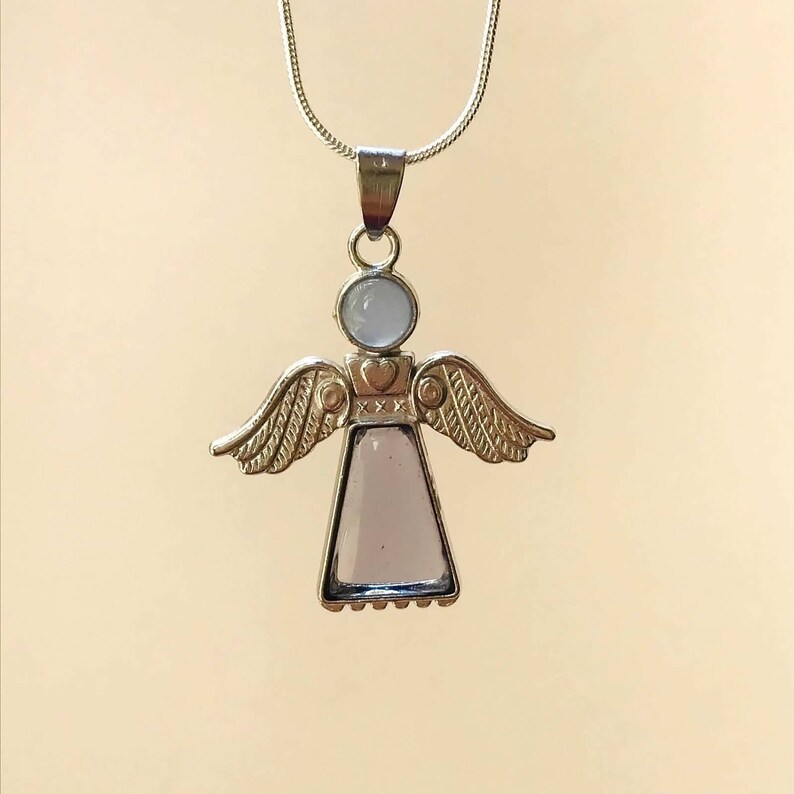 Op de afbeelding: Zilveren engel hanger ketting met een helder glazen lichaam en een witte steen op het hoofd. De vleugels zijn versierd met een hart en de letters 'XXX'.