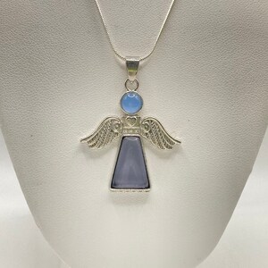 Op de afbeelding: Een zilveren engel hanger ketting met een lichtblauwe en paarse edelsteen. De engel heeft vleugels en een hart op zijn borst.