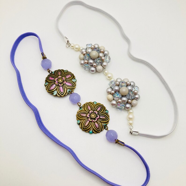 May include: A purple and white headband with two floral embellishments and a cluster of iridescent beads.