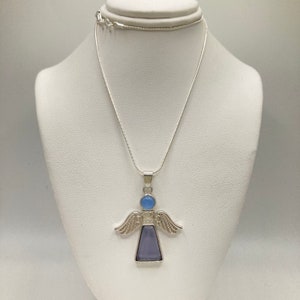Op de afbeelding: Een zilveren engel hanger ketting met een lichtblauwe en paarse edelsteen. De engel heeft vleugels en een hart op zijn borst.