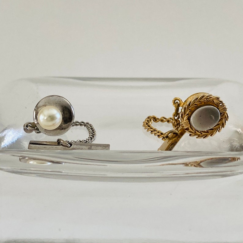 May include: Two tie tacks, one with a pearl and the other with a clear stone, both with silver and gold chains.