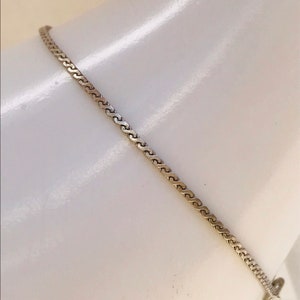May include: A silver chain necklace with a delicate, interwoven pattern. The chain is thin and has a subtle shine.