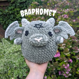 May include: Gray crocheted plush toy shaped like a goat with a pentagram on its forehead and the word "BAAPHOMET" above it.