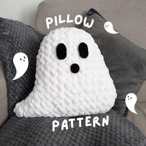 Könnte beinhalten: Ein weißes gehäkeltes Geisterkissen mit schwarzen Augen und einem Mund. Das Kissen liegt auf einer grauen, strukturierten Oberfläche mit den Worten "Pillow Pattern" in weiß.
