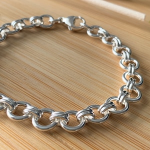 Puede incluir: Un brazalete de cadena de plata con cierre de langosta. La cadena est&aacute; hecha de c&iacute;rculos entrelazados.