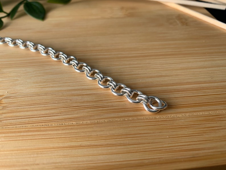 Puede incluir: Un brazalete de cadena de plata con un dise&ntilde;o delicado e intrincado. La cadena est&aacute; hecha de peque&ntilde;os c&iacute;rculos unidos que crean un aspecto suave y fluido.