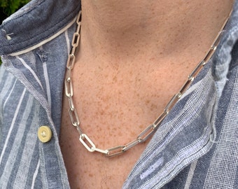 May include: A silver chain necklace with a link style. The chain is worn by a person with a light blue striped shirt.