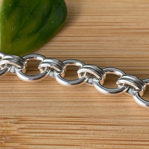 Puede incluir: Un brazalete de cadena de plata con un dise&ntilde;o &uacute;nico e entrelazado. La cadena est&aacute; hecha de eslabones redondos y gruesos que est&aacute;n conectados de una manera que crea una serie de peque&ntilde;os c&iacute;rculos superpuestos.