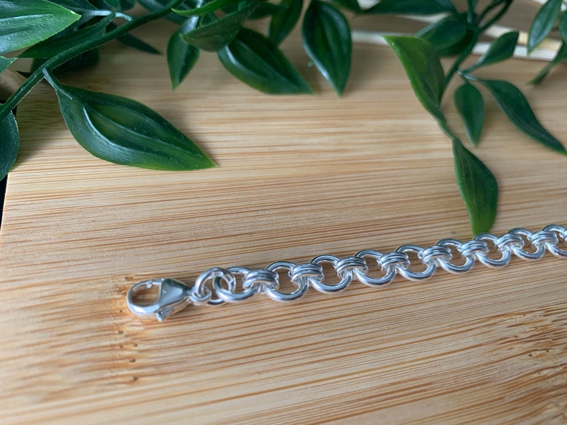 Puede incluir: Un brazalete de cadena de plata con cierre de mosquet&oacute;n. La cadena est&aacute; hecha de eslabones ovalados entrelazados.