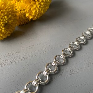 Puede incluir: Un brazalete de cadena de plata con un dise&ntilde;o entrelazado &uacute;nico. La cadena est&aacute; hecha de varios c&iacute;rculos peque&ntilde;os que est&aacute;n unidos para crear un brazalete resistente y duradero.