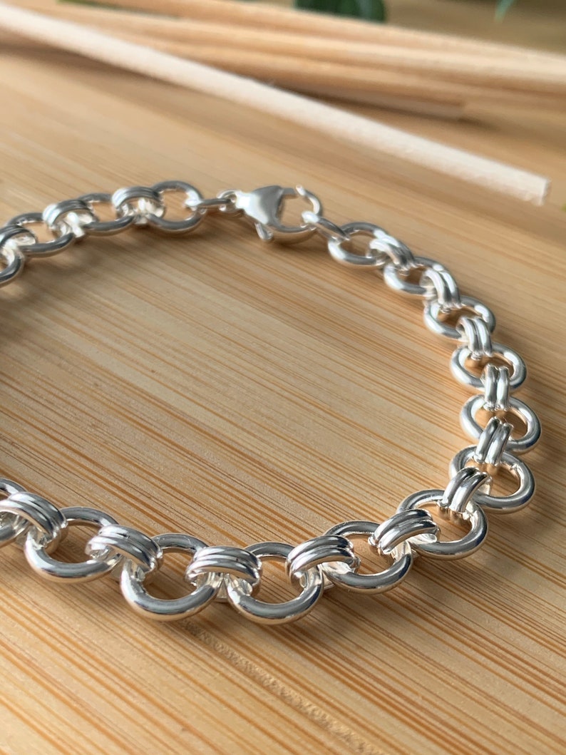 Puede incluir: Un brazalete de cadena de plata con cierre de langosta. La cadena est&aacute; hecha de c&iacute;rculos entrelazados.