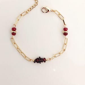 Puede incluir: Pulsera de cadena dorada con detalles de piedras preciosas rojas. La pulsera presenta una serie de eslabones rectangulares, con grupos de piedras preciosas rojas y un cierre de broche. Las piedras preciosas son de color rojo intenso.