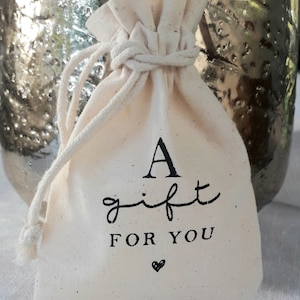 May include: A small white cotton drawstring bag with black text that reads "A gift for you" and a small heart.