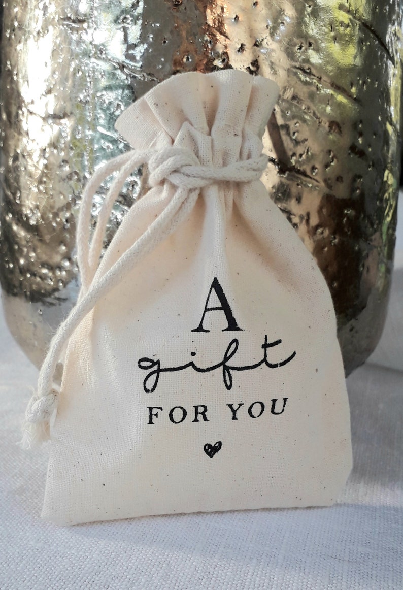 May include: A small white cotton drawstring bag with black text that reads "A gift for you" and a small heart.