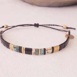 May include: A black and gold beaded bracelet with a black cord and gold beads. The bracelet has a small gold charm attached to it.