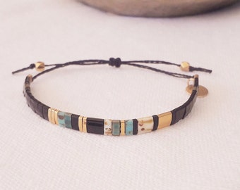 May include: A black and gold beaded bracelet with a black cord and gold beads. The bracelet has a small gold charm attached to it.