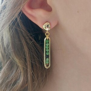 May include: Gold dangle earrings with a green and black bead design. The earrings have a small gold teardrop shape at the top.