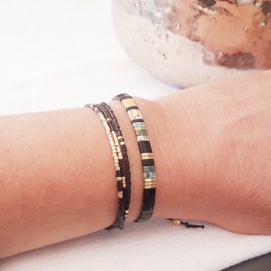 May include: A set of three bracelets with black, gold, and turquoise beads. The bracelets are stacked on a person's wrist.