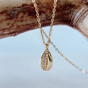 May include: A gold chain necklace with a small seashell pendant. The seashell is decorated with clear rhinestones.