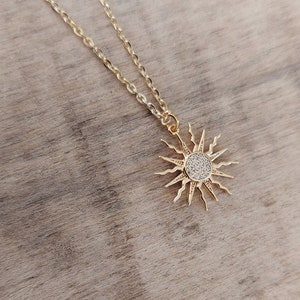 Peut inclure: Un collier en chaîne dorée avec un pendentif en forme de soleil. Le soleil est en or et est serti de petites pierres claires.