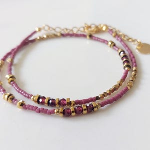 May include: A double-strand bracelet with mauve beads and gold accents. The bracelet features small, dark purple gemstones.