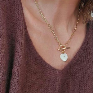 Peut inclure: Un collier en chaîne dorée avec un fermoir à bascule et un pendentif en forme de cœur blanc avec un petit strass.