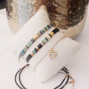 May include: Three bracelets with black and gold beads, one with turquoise and gold beads, and a gold chain with a circular pendant.