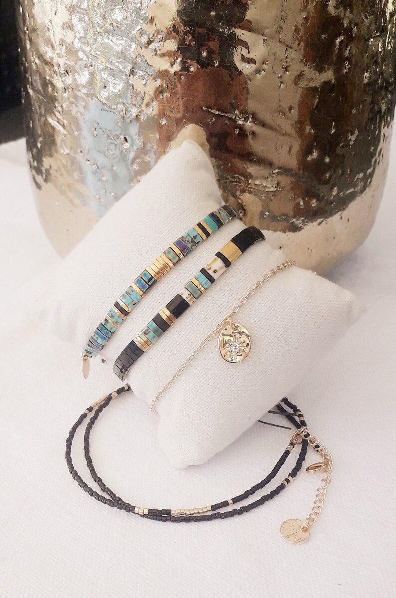 May include: Three bracelets with black and gold beads, one with turquoise and gold beads, and a gold chain with a circular pendant.
