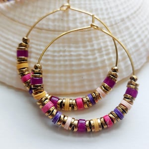 May include: A pair of gold hoop earrings featuring a repeating pattern of small, flat, circular beads in shades of magenta, purple, yellow, and pale pink, interspersed with metallic gold-toned spacer beads along the lower half of each hoop.