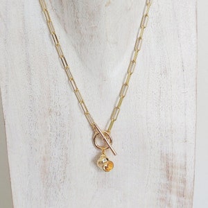 May include: A gold chain necklace with a toggle clasp and a small seashell pendant.