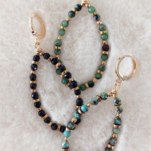 Peut inclure: Trois paires de boucles d'oreilles créoles dorées avec des perles de pierres précieuses. Les boucles d'oreilles présentent des perles noires, vertes et turquoise.