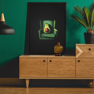 May include: A framed illustration of an avocado sitting in a green armchair against a black background. The avocado has a smiling face and is sitting in a green armchair. The illustration is on a wooden shelf with a brown bottle and a potted plant.