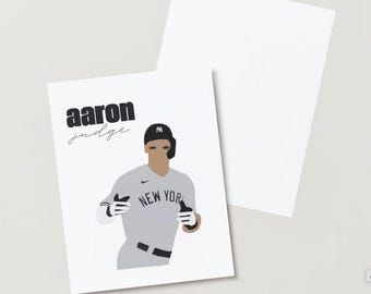 May include: A white print featuring a stylized illustration of baseball player Aaron Judge in a New York Yankees uniform. The print includes the text "Aaron Judge" in bold and script fonts.