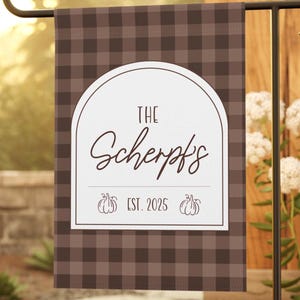 May include: A rectangular garden flag featuring a brown and dark brown buffalo plaid pattern. The center displays a white arched design with the text "THE Scherpf's" and "EST. 2025" accompanied by two small pumpkin illustrations.