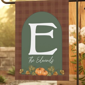 Peut inclure: Un drapeau de jardin rectangulaire avec une bordure à carreaux marron et un centre arqué vert sauge. Le drapeau présente une grande lettre E blanche, le texte The Edwards en écriture blanche et un motif de citrouilles orange avec des feuilles vertes.