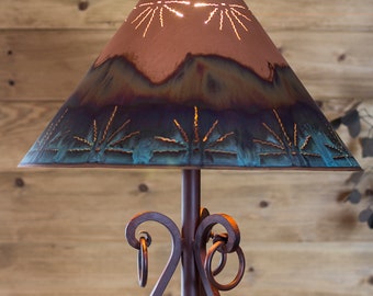 May include: A rustic metal floor lamp with a decorative, teal and brown, cut-out metal lampshade. The lampshade has a southwestern design.