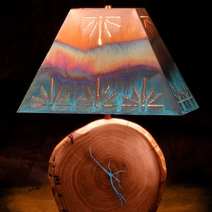May include: A lamp with a copper and turquoise patterned shade and a wooden base. The shade has a geometric design with a sunburst pattern in the center.